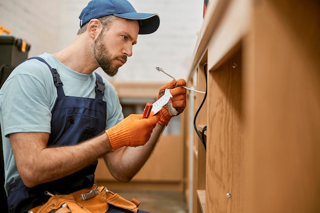 Bearded male electrician fixing desk electrical wires