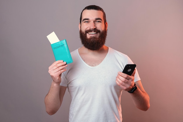 Бородатый студент готов к поездке Он держит телефон и паспорт
