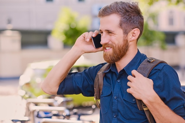 古いヨーロッパの町でスマートフォンで話すバックパックを持つひげを生やした男性。