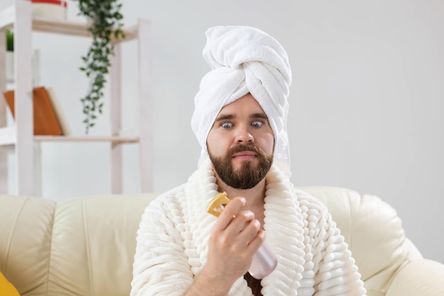 Bearded male with bath towel on his head applying spray water treatment on face spa body and skin