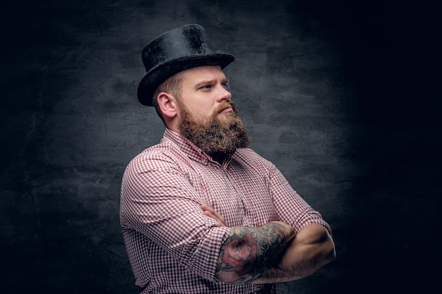 Bearded male with crossed tattooed arms wearing top hat.