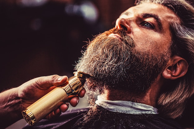 Photo bearded man in barbershop. man visiting hairstylist in barbershop. barber works with a beard clipper. hipster client getting haircut.