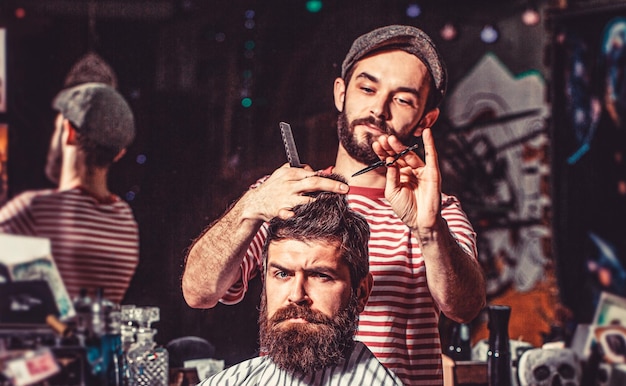 Foto uomo barbuto nel negozio di barbiere lavoro nel negozio di barbiere parrucchiere che taglia i capelli del cliente maschio parrucchiere che serve cliente al negozio di barbiere uomo in visita parrucchiere nel negozio di barbiere