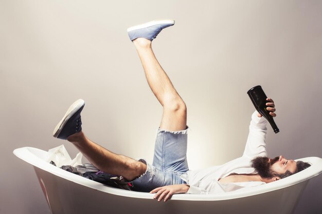 Bearded man in bathtub with bottle