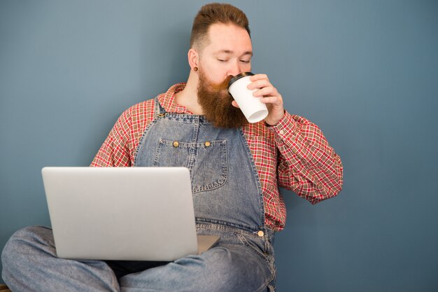 Bearded man in blue overalls drinking coffee