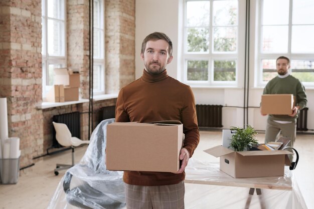 Bearded man bringing box of office stuff in new office