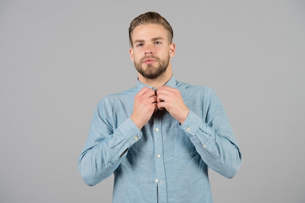 Bearded man button blue shirt. Man with beard on unshaven face skin. Fashion model in casual outfit on grey background. Style or trend and vogue concept. Skincare and barber salon.