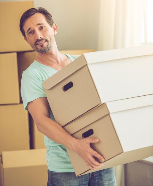 Bearded man in casual clothes is carrying boxes.