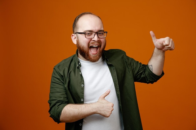 Bearded man in casual clothes looking at camera crazy happy showing thumbs up smiling standing over orange background