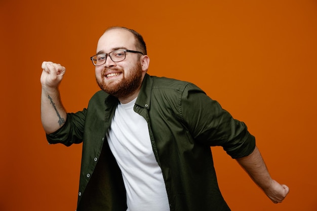 Bearded man in casual clothes standing over happy and excited clenching fists rejoicing his success orange background