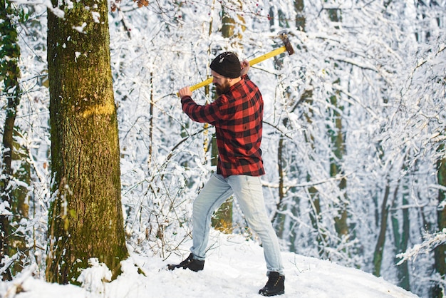 Bearded man chopping a tree. Bearded lumberjack. Brutal bearded lumberjack with ax in winter forest. Handsome man, hipster in snowy forest. Lumberjack with an ax in his hands.