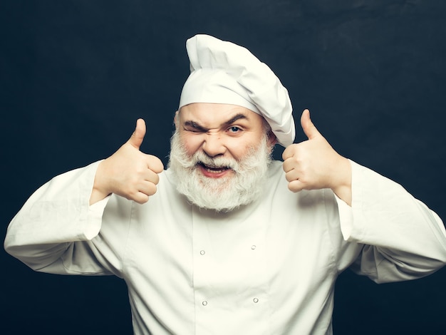 Bearded man cook with winking face in chef hat with thumb up in studio on black background