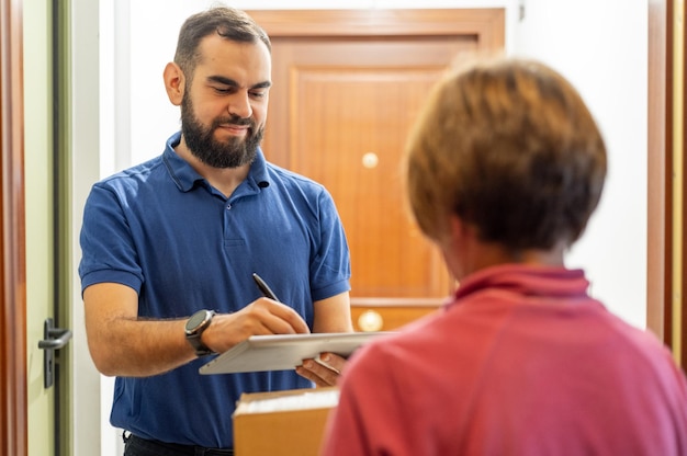 Photo bearded man delivering a package to a lady signing on a tablet