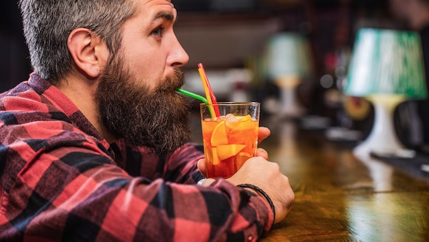 あごひげを生やした男はカクテルを飲みます。トロピカルアルコールのフレッシュカクテル。あごひげを生やしたカクテル。オレンジジュースを飲む肖像画の男。