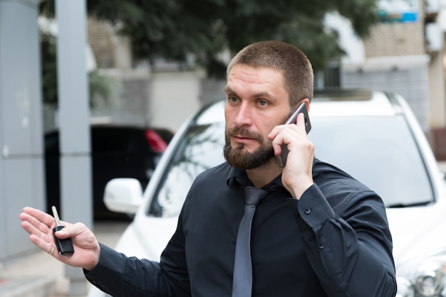 Bearded man emotionally talking on the phone near the car