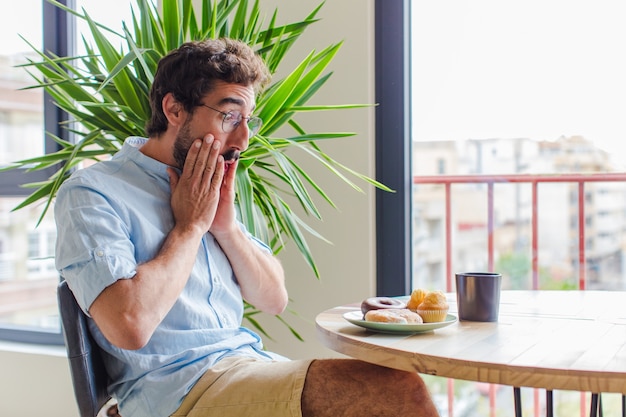 Bearded man feeling shocked and scared, looking terrified with open mouth and hands on cheeks