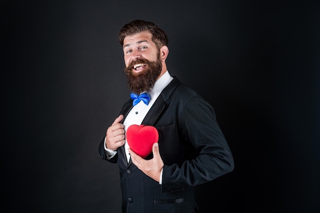 Bearded man in formal tuxedo with bow tie share love heart at\
14th february valentines day love