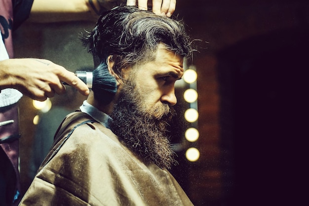 Bearded man getting powder on skin with makeup brush