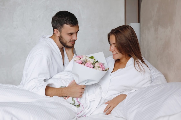 Bearded man gives a bouquet of flowers to a woman in a white bed
