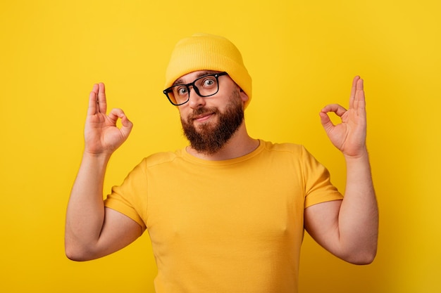 Bearded man in glasses showing ok gesture over yellow background