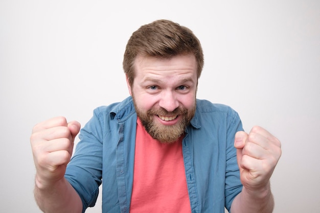 Photo bearded man happily smiles and clenched his fists showing success and victory