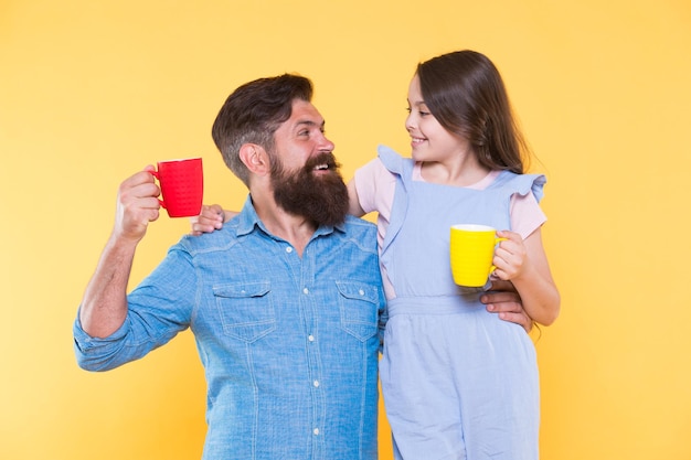 Bearded man and happy girl holding mugs Father and daughter hot drink Drink water Drink fresh juice Breakfast concept Good morning Having coffee together Healthy lifestyle Family drinking tea