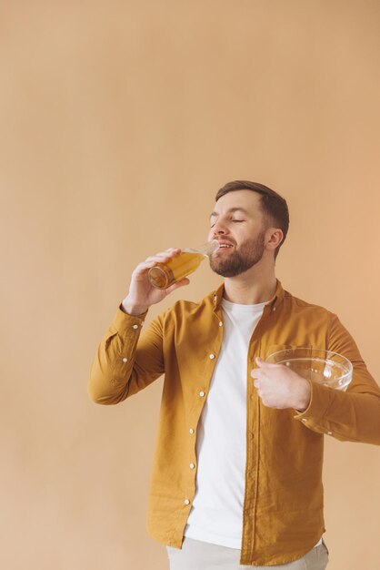 Bearded man happy and smiling in yellow shirt drinking beer and eating chips on beige background