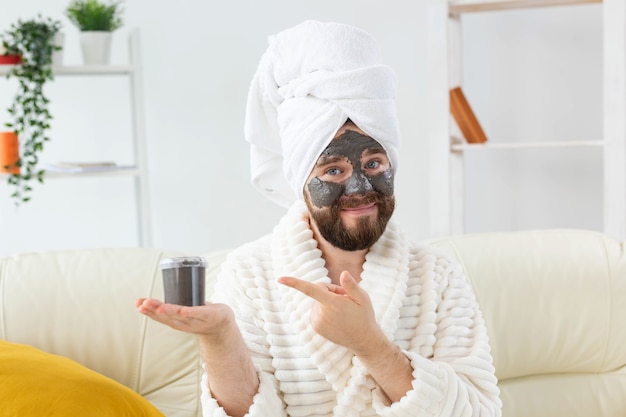Bearded man having fun with a cosmetic mask on his face made from black clay men skin care humor and