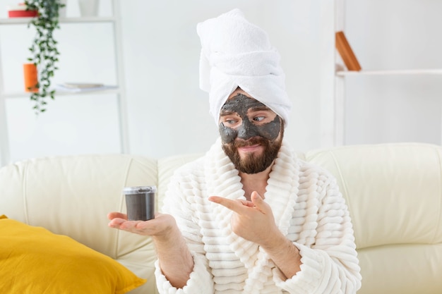 Bearded man having fun with a cosmetic mask on his face made from black clay men skin care humor and