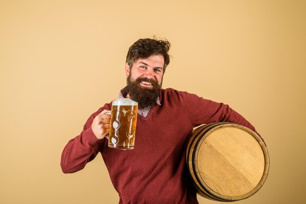 Bearded man hold glass and barrel with craft beer attractive bearded brewer with wooden barrel of