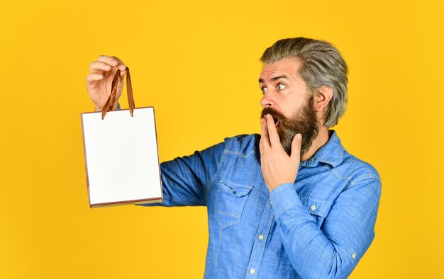 Bearded man hold paper bag presents delighted man shopping online surprised hipster making purchases at electronics store Positive man enjoying shopping Own business Choosing the best