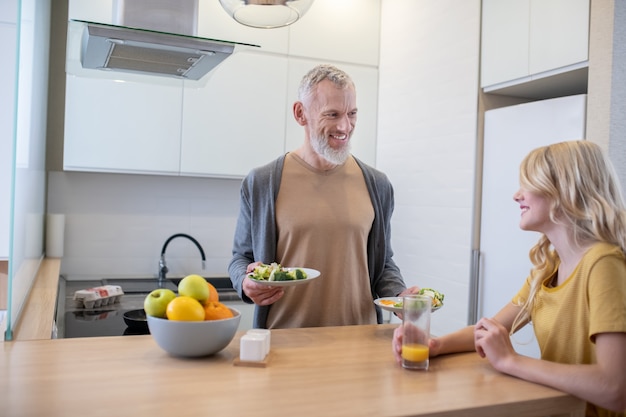 A bearded man holding two plates and offering food to his daughter