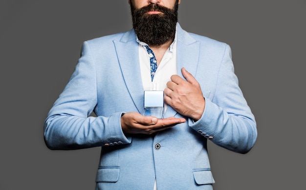 Bearded man holding up bottle of perfume. Perfume or cologne bottle and perfumery, scent cologne bottle. Masculine perfume, bearded man in a suit. Male holding up bottle of perfume in suit.