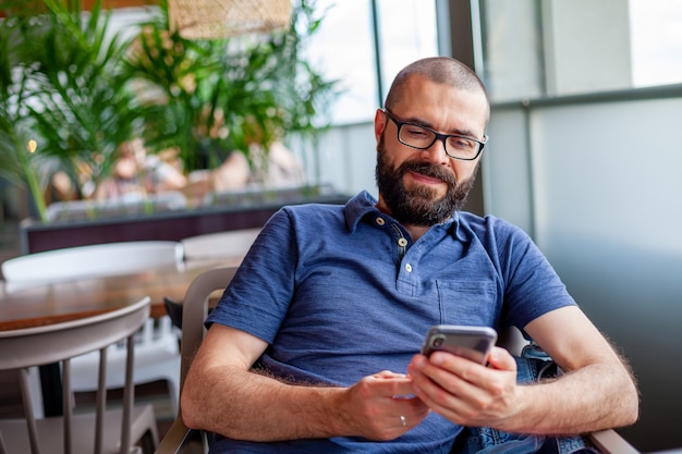 Bearded man holding and using smartphone for sms messages, typing touchscreen cell phone in the cafe. Lifestyle, technology and Social media network concept.