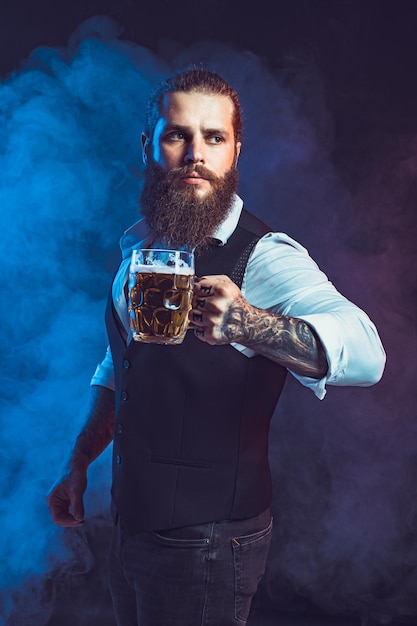 Бородатый мужчина держит в руке вкусное разливное пиво на фоне дыма, пьет концепцию октябрьского фестиваля
