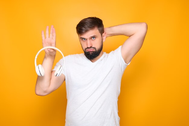 Bearded man holds white headphones in his hand and pouted his lips.