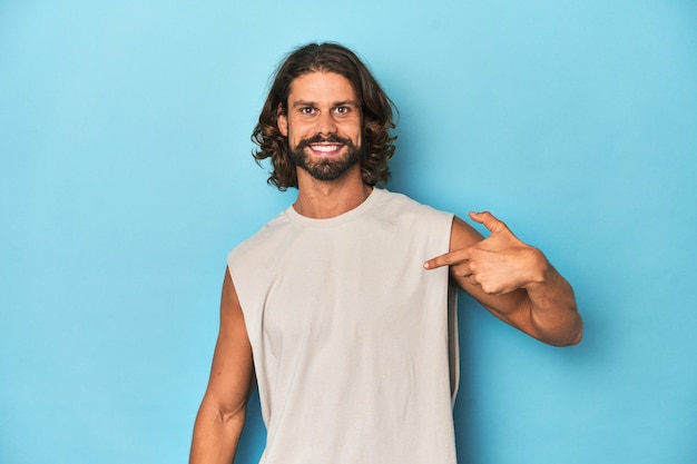 Bearded man in een tank top blauwe achtergrond persoon wijzen met de hand op een shirt kopieer ruimte trots