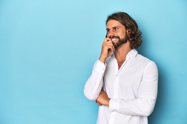 Bearded man in een wit hemd blauwe achtergrond ontspannen nadenken over iets kijken naar een kopie ruimte