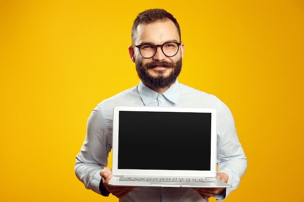 Бородатый мужчина в очках и бежевой рубашке показывает новый современный ноутбук
