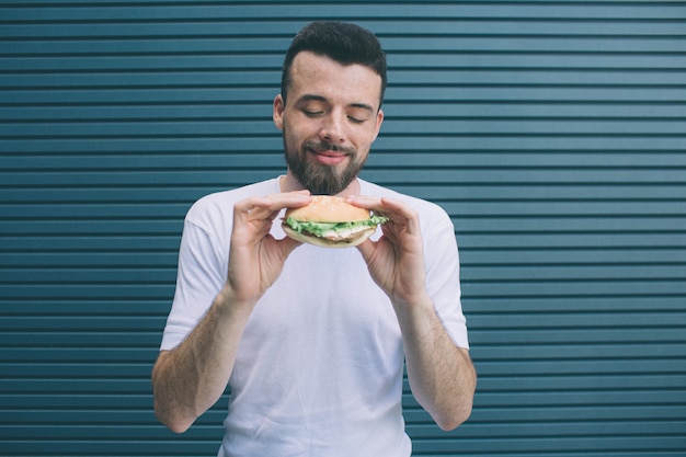 Bearded man is holding burger with both hands. He is looking at it and smiling. Isolated on striped 