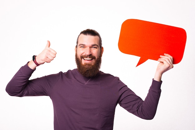 Bearded man is holding a speech bubble and smiling is showing a thumb up