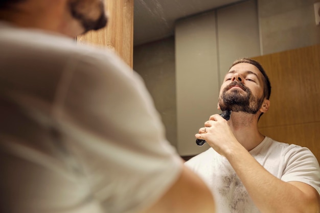 수염난 남자가 화장실에서 면도기로 수염을 깎고 있다