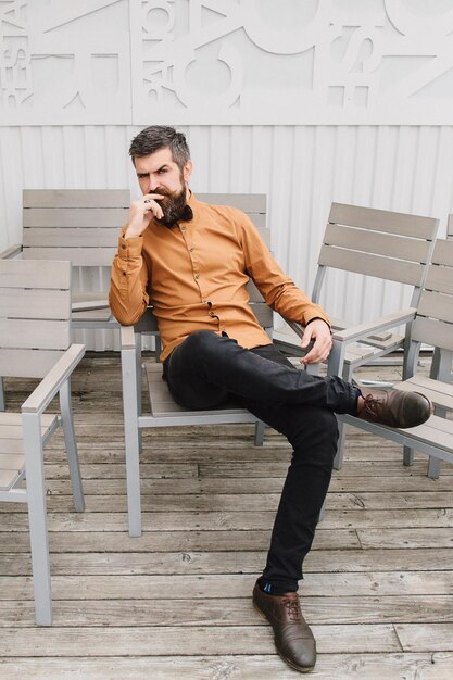 A bearded man is sitting on a chair and next to him a lot of empty