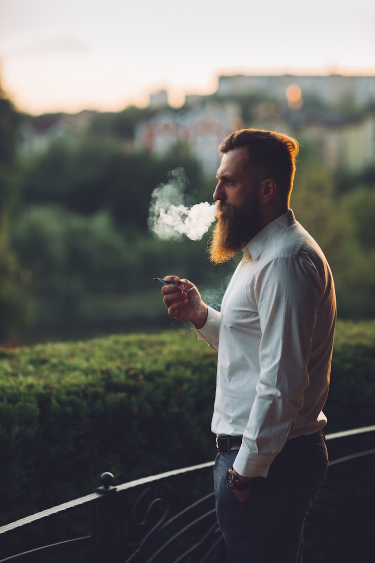 Photo a bearded man is smoking a cigarette against the sunset.