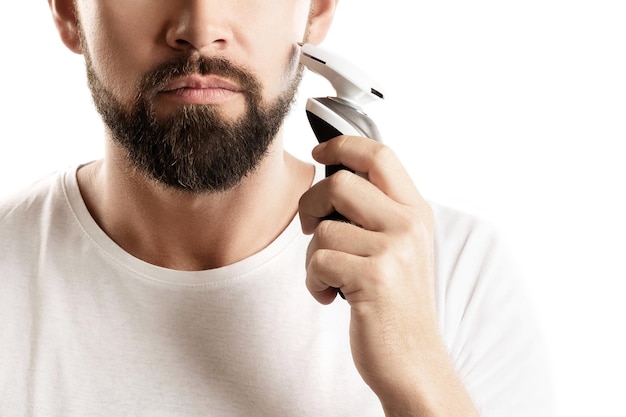 Bearded man is using electric trimmer on white background