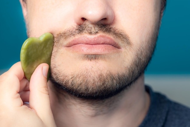 L'uomo barbuto sta usando il rullo facciale di giada