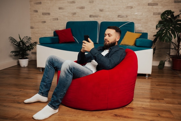 Bearded man is using phone in modern living room.