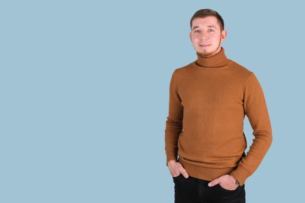 Photo a bearded man laughs with his hands in his pockets and standing on a blue background, copyspace