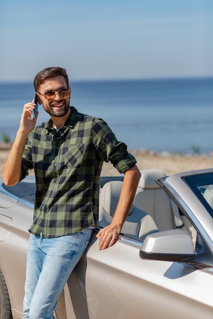 Bearded man leaning the cabriolet and talking on smartphone