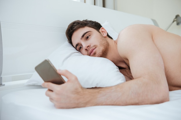 Bearded Man lying on bed and using phone